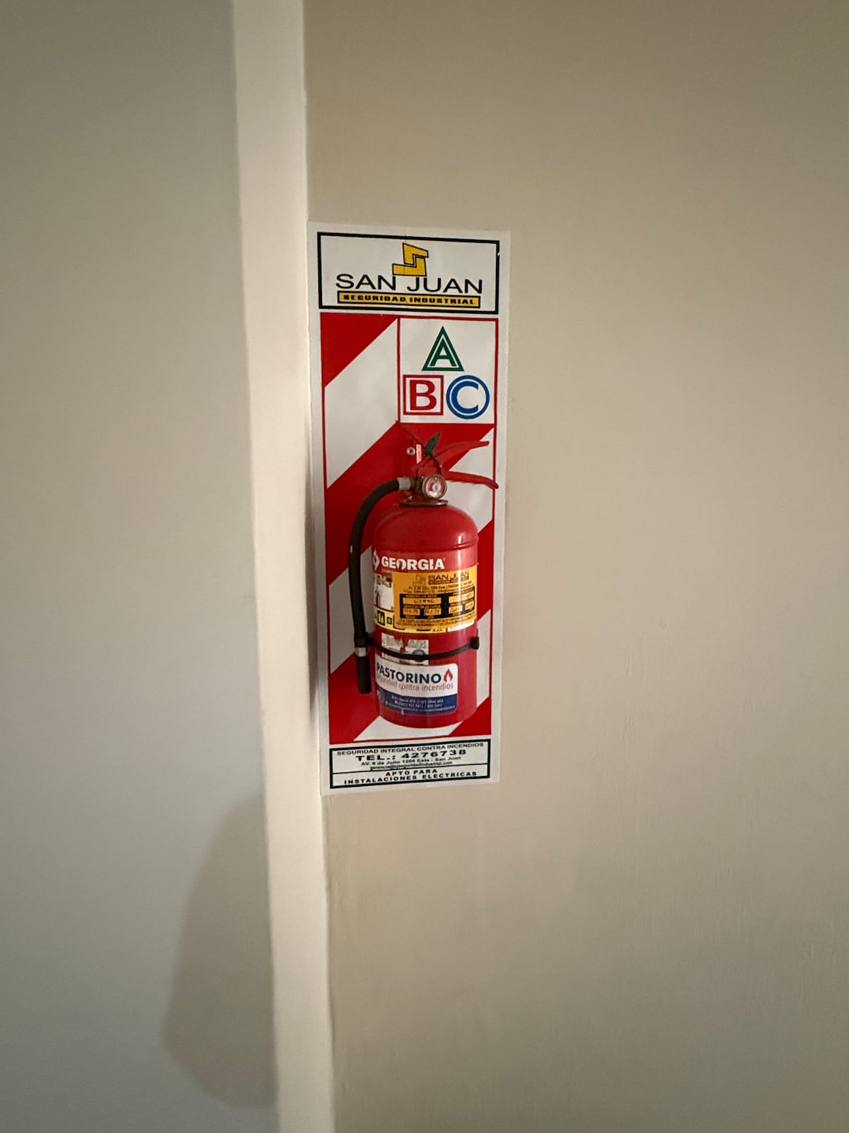 A fire extinguisher is mounted on a wall with a red and white striped sign for visibility. The extinguisher is clearly marked, ensuring easy access in case of an emergency, and is positioned near the floor to ensure compliance with safety regulations.