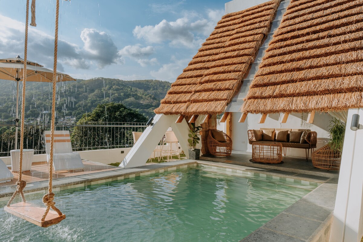 A serene pool area is shown, surrounded by modern design elements. The structure features a thatched roof and cozy seating arrangements. A swing hangs above the pool, complemented by a sun umbrella and views of the surrounding nature.