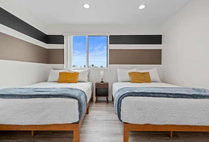 Dos cómodas camas tamaño queen con iluminación natural y mesita de noche. 