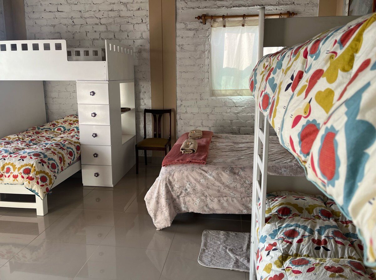 Diseñada pensando en el descanso y la comodidad de grupos grandes o familias, esta espaciosa habitación cuenta con cinco camas distribuidas inteligentemente para aprovechar cada rincón sin perder amplitud.