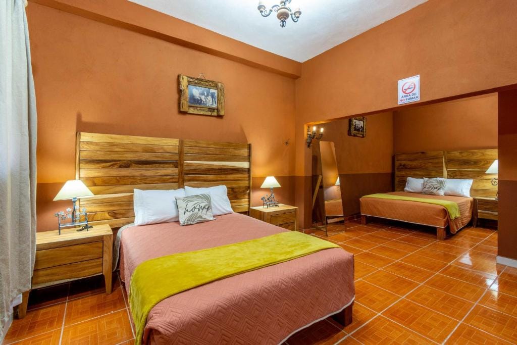 A cozy sleeping area is showcased with warm, earthy tones on the walls. A spacious bed is adorned with muted bedding and a vibrant green throw. Two bed-side lamps provide gentle lighting, and a mirror reflects the inviting atmosphere of the room.