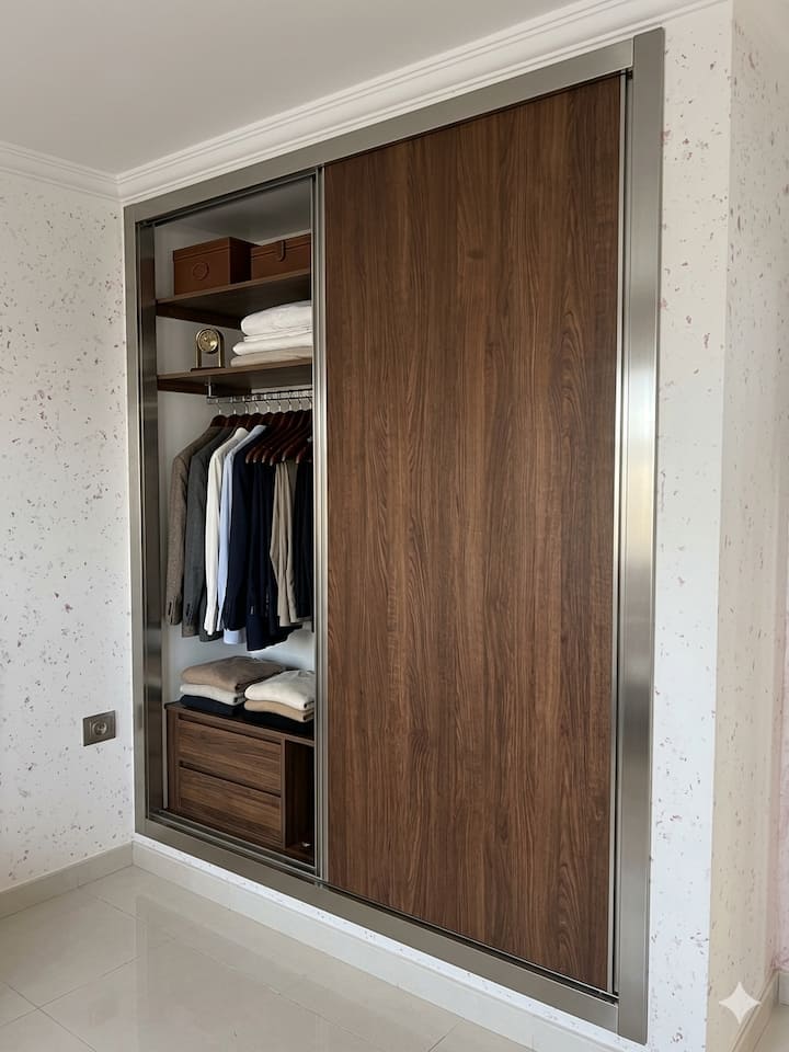 Vestiário de quarto moderno e elegante. Portas deslizantes que economizam tempo, acabamento aconchegante em nogueira e estrutura cromada. Organização otimizada: guarda-roupa, gavetas, prateleiras e cômoda. Perfeito para guardar roupas e acessórios