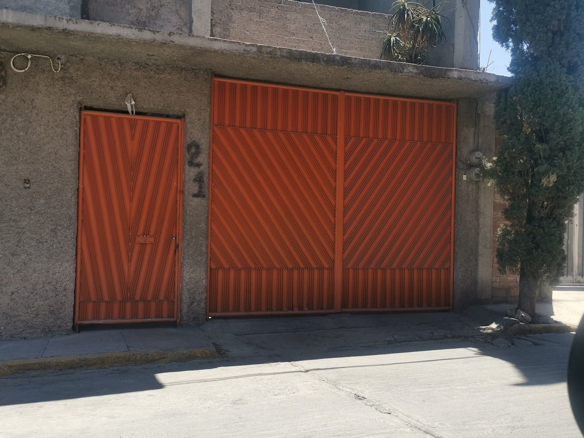 The entrance features a large orange gate complemented by a smaller matching door to the left. The facade displays a textured, gray surface, and numbers '21' are visible on the wall, serving as a clear point of identification.