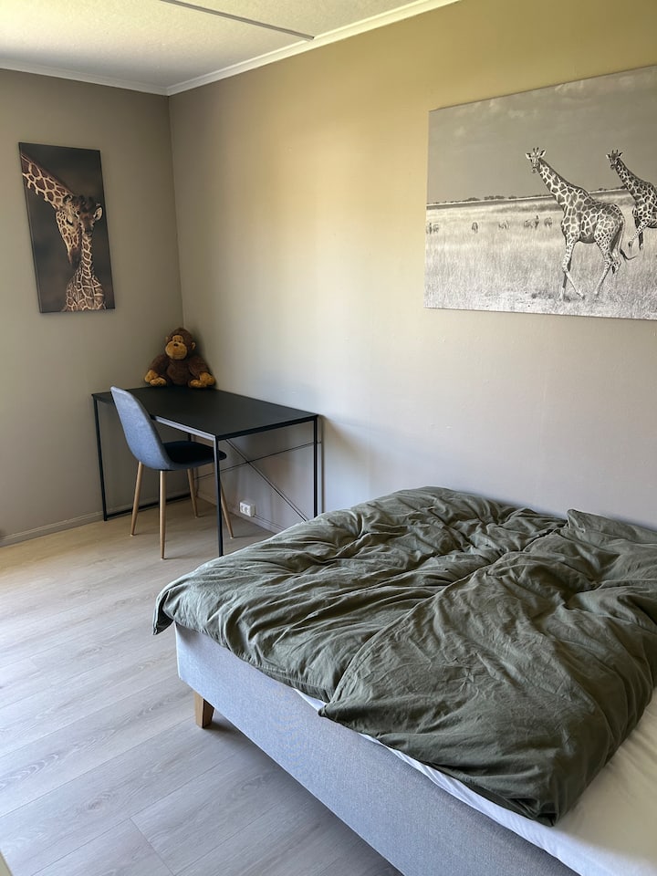 La habitación de la jirafa. Contiene una cama de 120 cm, una cómoda grande, mesitas de noche, un escritorio y una vista al jardín. Grandes ventanas con persianas enrollables opacas. 