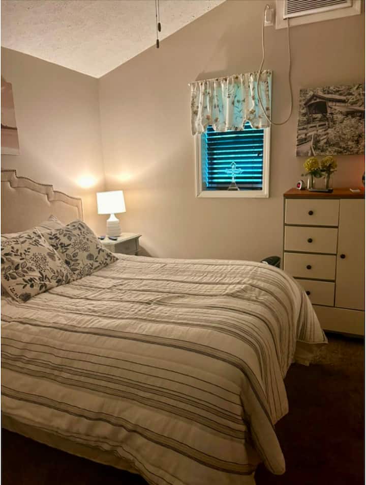 מיטה בגודל מלא עם כל המצעים ויחידת מיזוג אוויר בחלון.