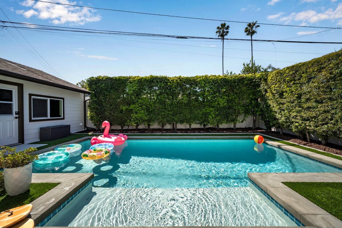 A sparkling pool is surrounded by lush greenery, creating a private oasis. Colorful floaties and a beach ball rest gently on the water's surface, inviting leisurely relaxation. The pool area is framed by clean, modern landscaping and a well-maintained exterior of the home.