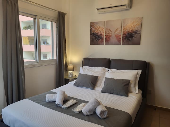 Oaza mira: veliki bračni krevet sa sivim uzglavljem, svježa bijela posteljina, sivi detalji, ručnici i papuče. Umjetnička djela s motivom zlatnih anđeoskih krila, pogled na grad, tihi klima-uređaj, veliki ormar. Čisto, moderno i opuštajuće.