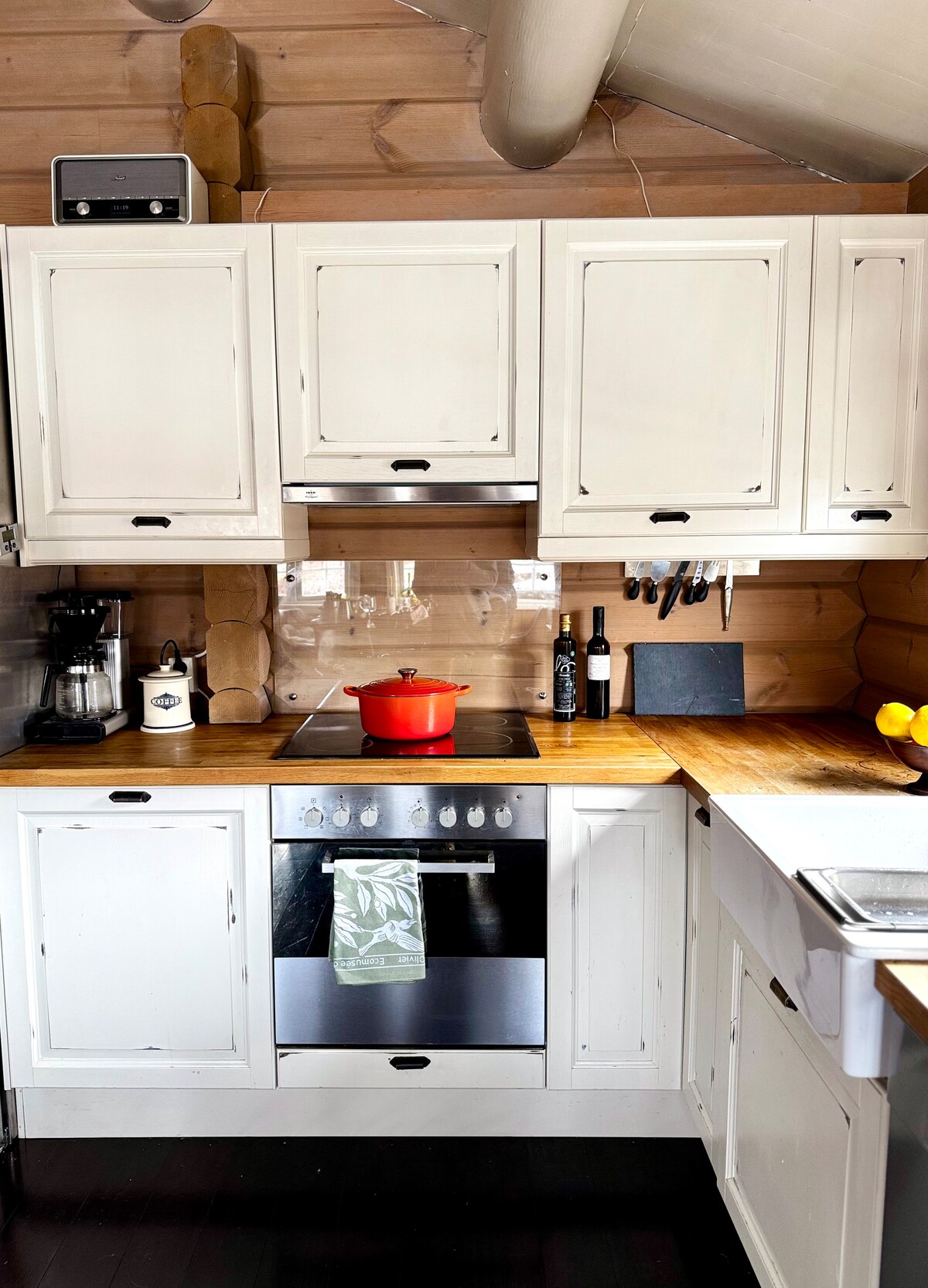 A fully equipped kitchen is presented with light-colored cabinetry and a warm wooden countertop. A modern stove and oven are featured, alongside small appliances like a coffee maker. Cooking utensils hang neatly on the wall, and a red pot adds a pop of color to the inviting space.