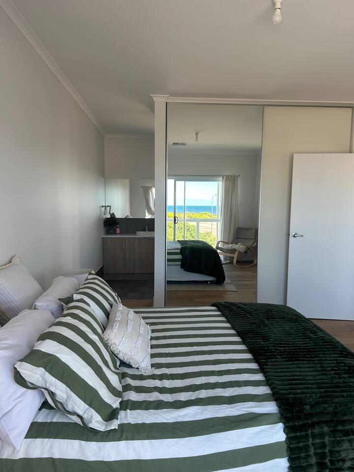 חדר שינה ראשי למעלה עם מיטת קווין סייז, סוויטה מלאה ונוף לים. 