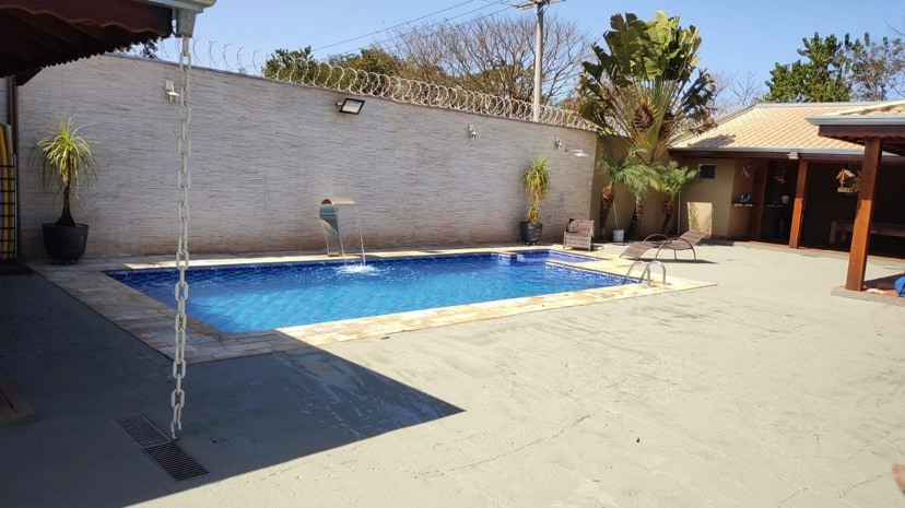 An outdoor area features a serene swimming pool surrounded by palm trees and lounge chairs. A spacious patio provides ample room for relaxation, with sunlight reflecting off the water's surface. The surroundings are calm, enhancing the tranquil atmosphere of the space.