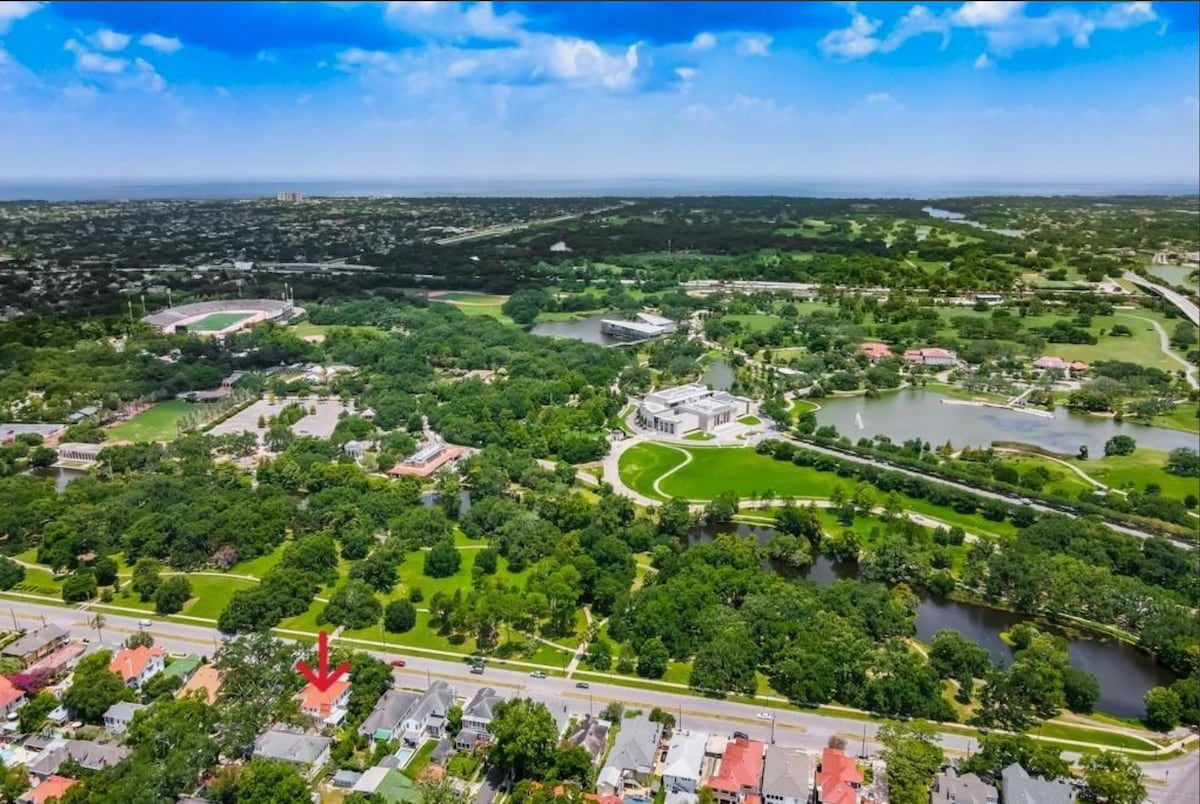 An aerial view captures a lush landscape of greenery with various trees and open spaces. The proximity to urban areas is evident, with residential buildings lining the bottom of the image. The nearby waterways and parks highlight the peaceful surroundings and connectivity to the city.