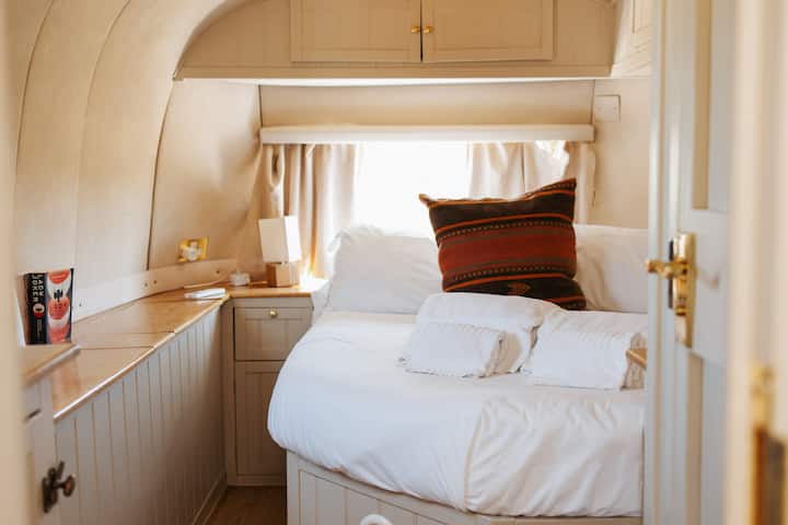 Cozy up in this bright Airstream bedroom, featuring a plush queen bed, premium linens, and clever built-in storage. A perfect blend of minimalist design and high-end glamping comfort for a restful night's sleep.
