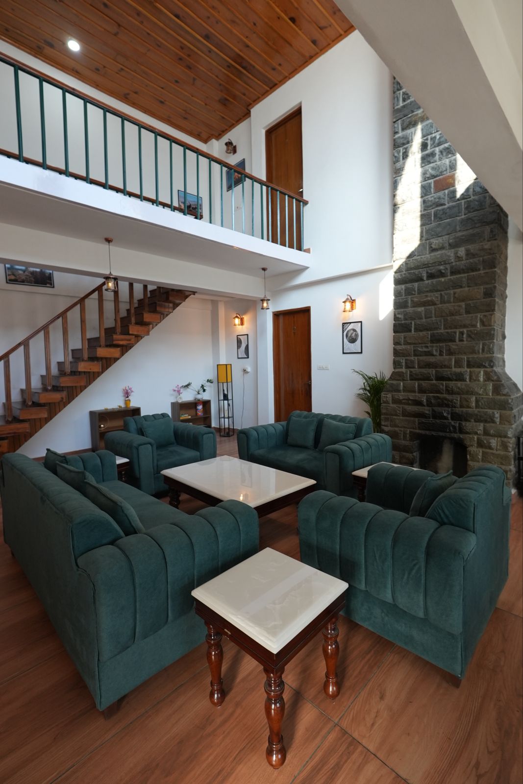 Double-height living room — stone fireplace, exposed beams, green velvet