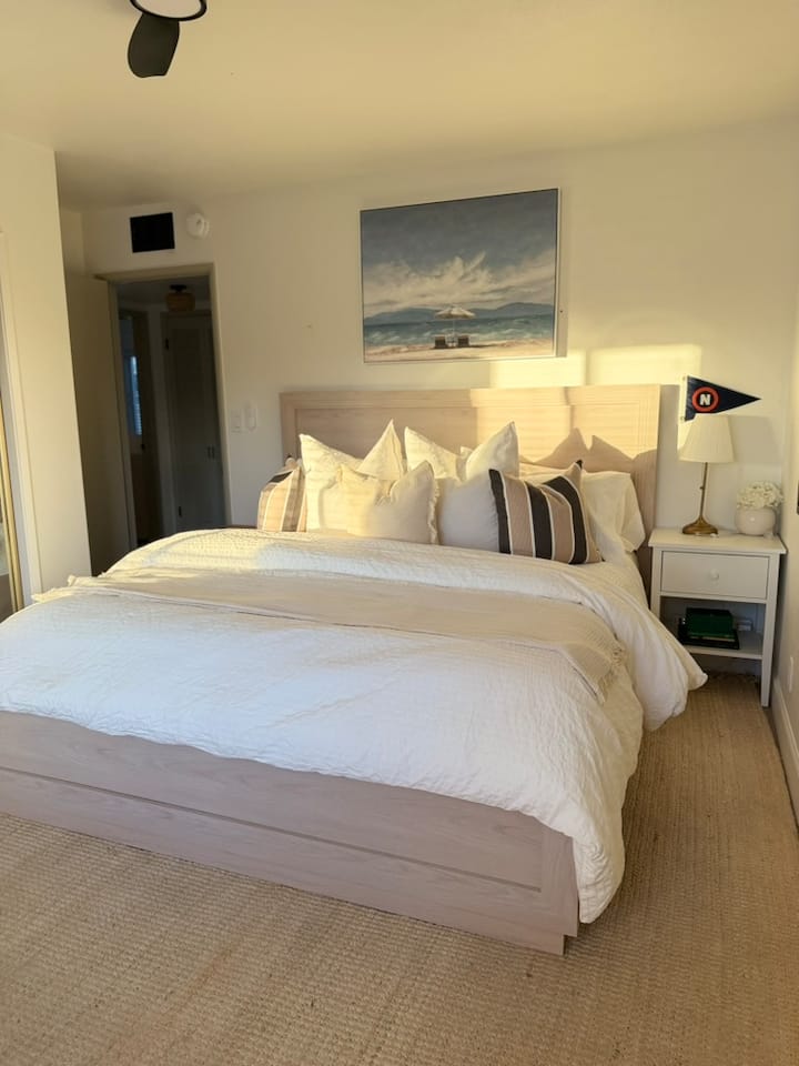 Lit king size confortable avec draps frais, ambiance côtière et belle lumière du soleil de l'après-midi