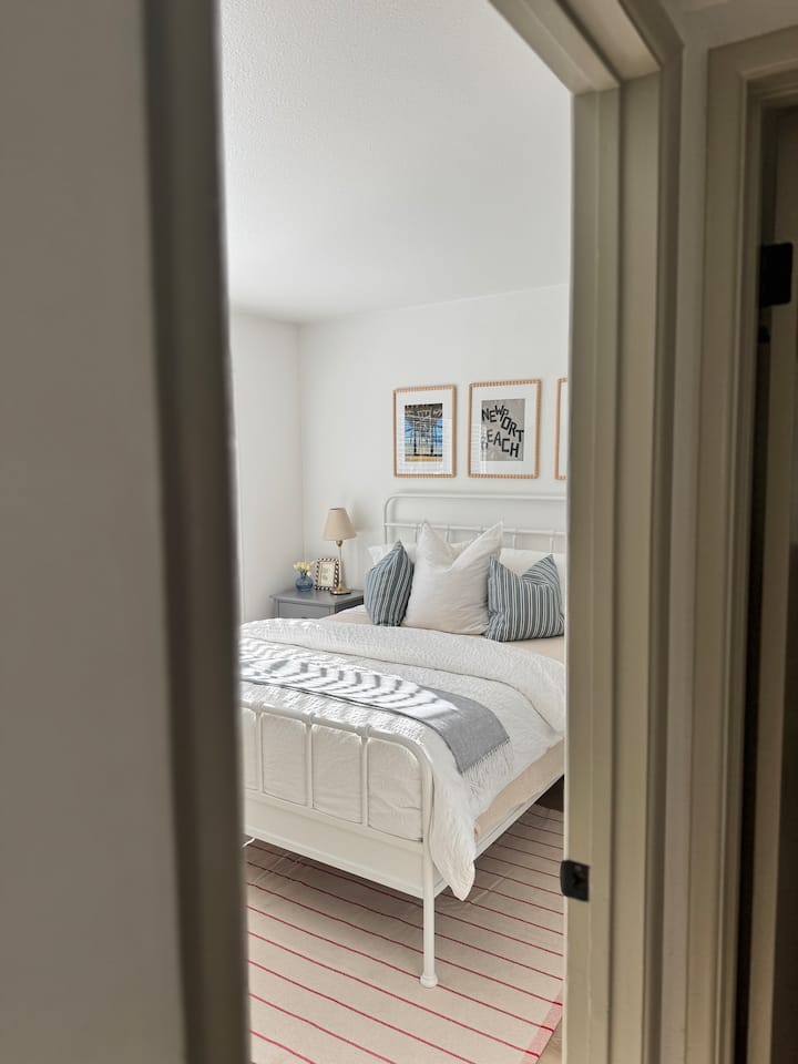 Un aperçu de la chambre queen avec beaucoup de lumière naturelle, des draps impeccables et des détails côtiers