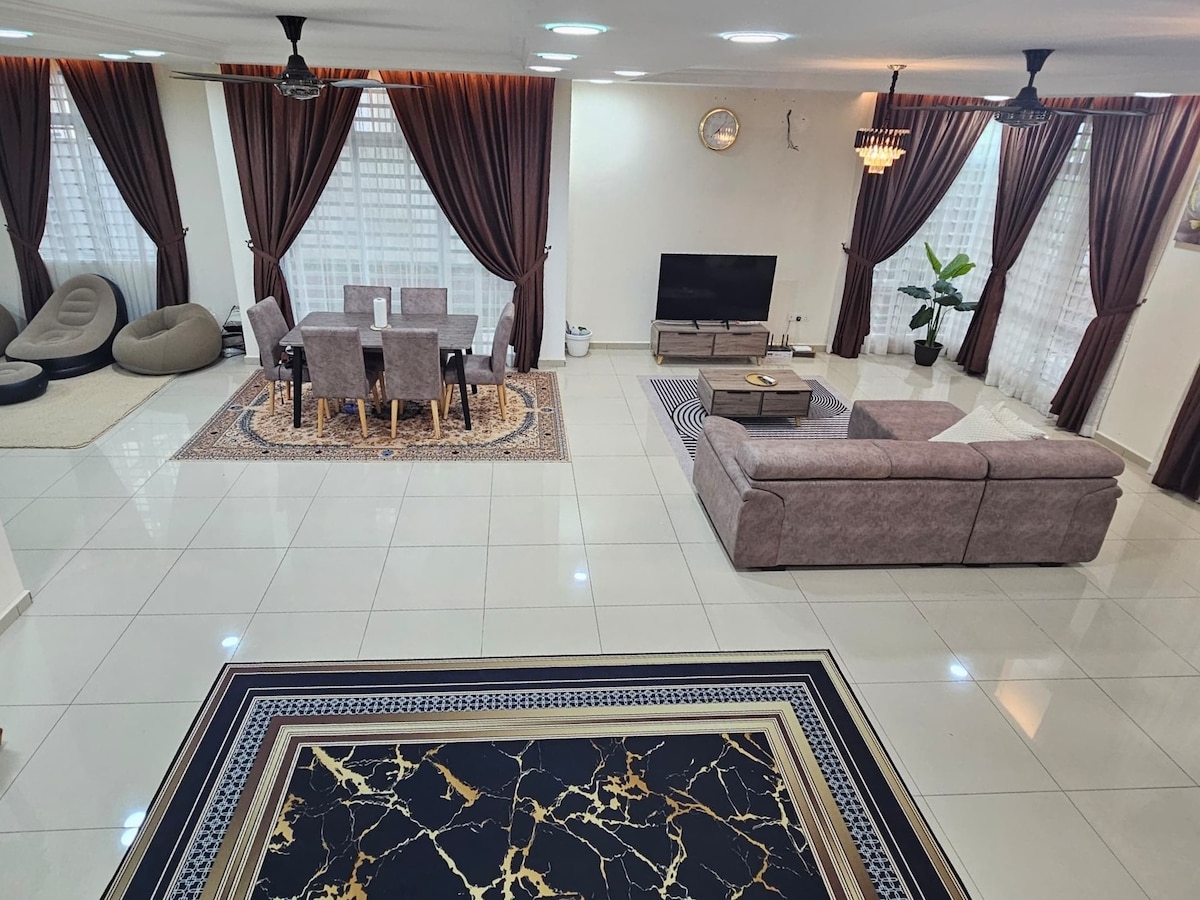 An open living space showcases a large sectional sofa and a dining area with a rectangular table surrounded by chairs. Natural light filters through large windows, with elegant curtains framing the view. A flat-screen TV is positioned against the wall, alongside a decorative plant.