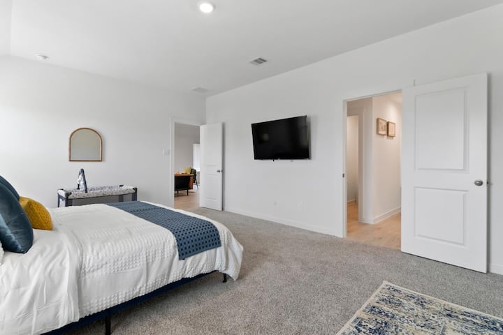 Descripción general del dormitorio principal: amplio dormitorio principal con una cama tamaño king, alfombras suaves, iluminación empotrada y un televisor montado en la pared para mayor comodidad.