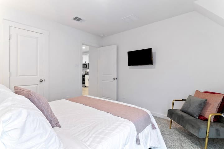 Descripción general del dormitorio 3: cómodo dormitorio con una cama tamaño queen, TV montada en la pared, alfombras suaves y un diseño limpio y moderno.