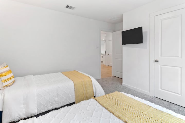 Descripción general del dormitorio 4: dormitorio luminoso y cómodo con dos camas individuales, alfombras suaves y un televisor montado en la pared para el entretenimiento.