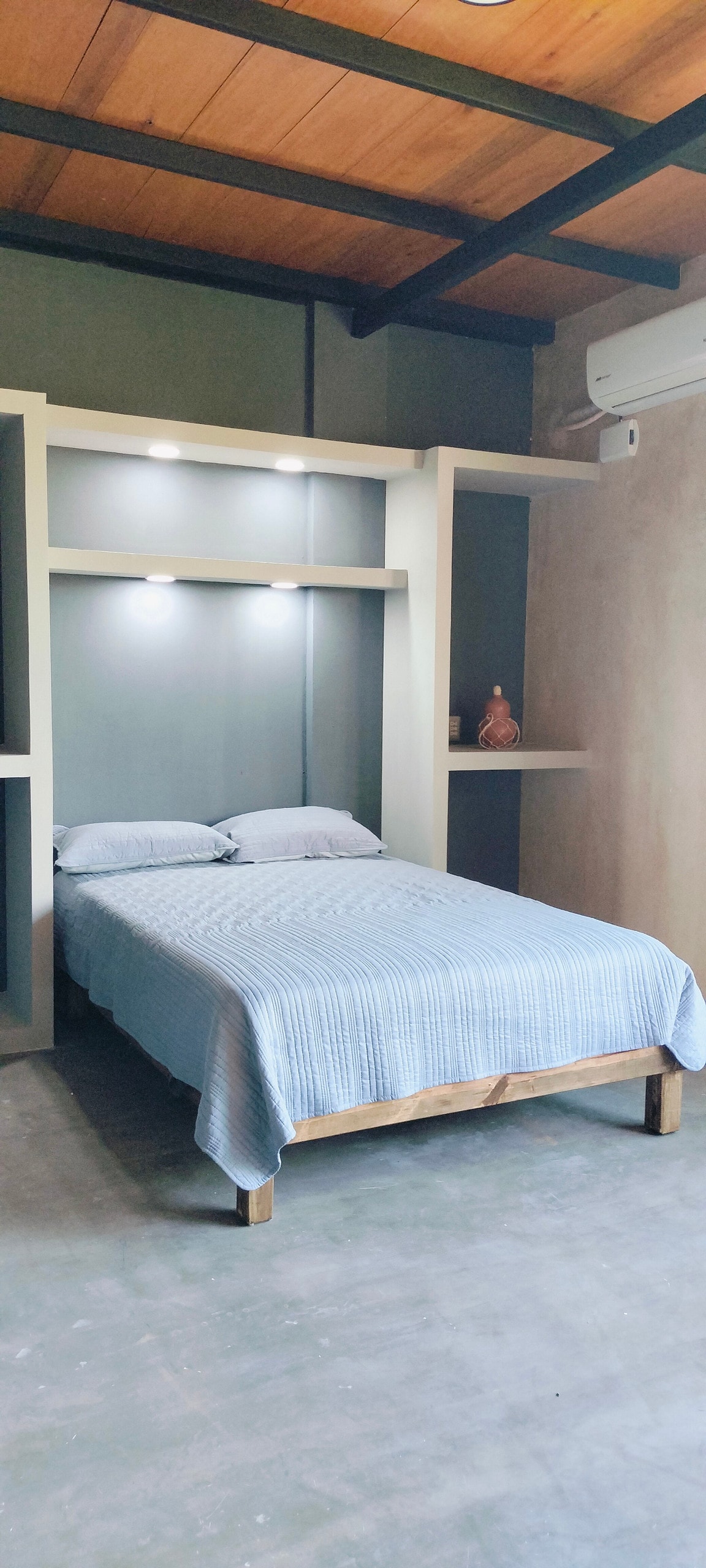 A spacious sleeping area is featured, showcasing a bed with a light striped blanket. Soft lighting is provided by mounted fixtures above the bed, and minimalist shelving units surround the sleeping space, enhancing the clean, modern look.