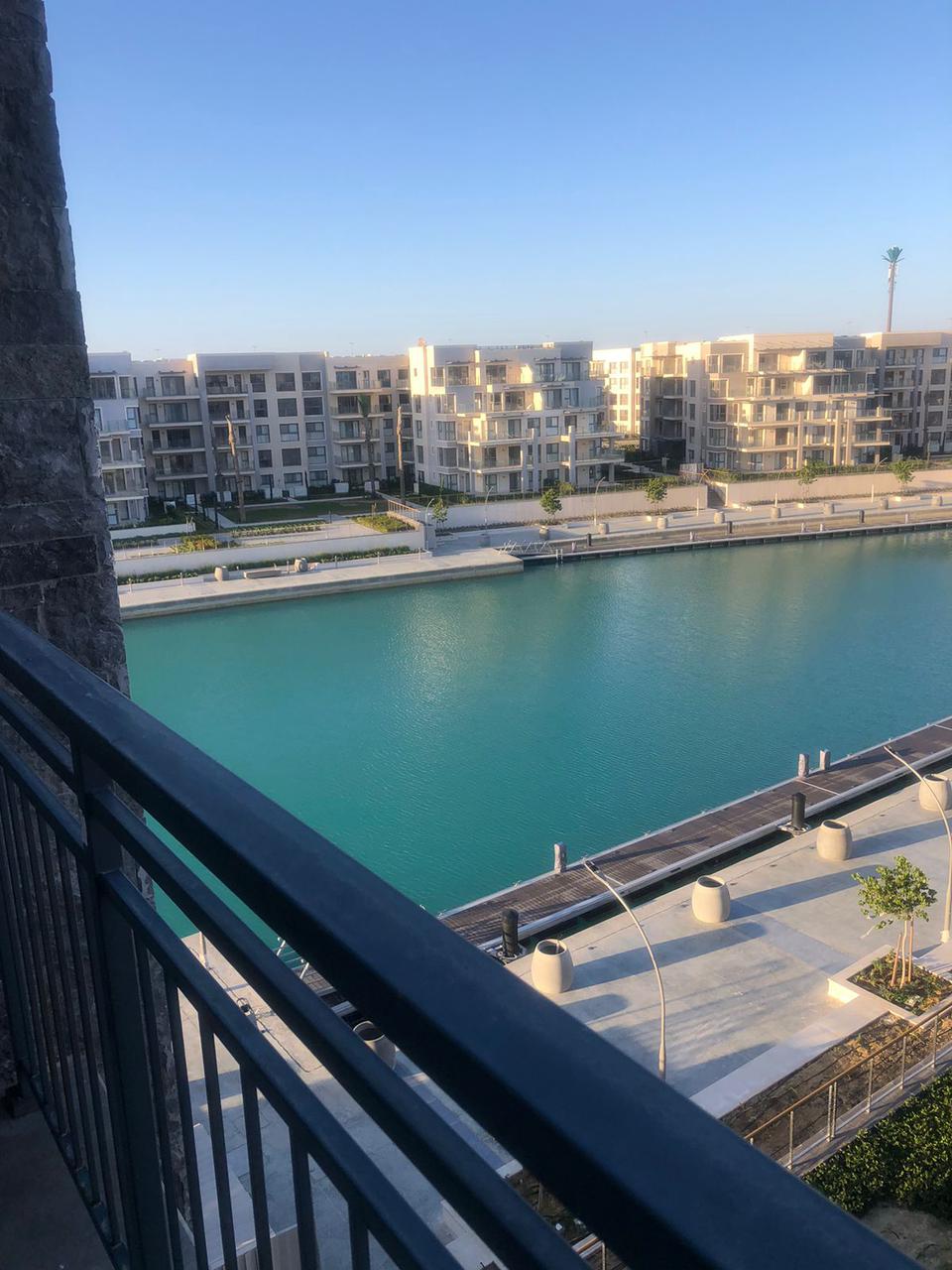 A tranquil view of a marina is presented, featuring calm turquoise waters bordered by modern residential buildings. The scene reflects clean lines and a well-maintained environment, with landscaped areas subtly integrated alongside the waterway.