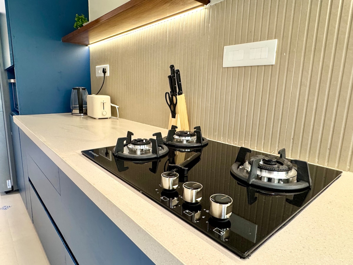 The modern kitchen features a sleek gas stove with three burners set against a textured wall. Nearby, kitchen utensils are neatly arranged in holders, with a stylish countertop illuminated by warm under-cabinet lighting, enhancing the practical design.