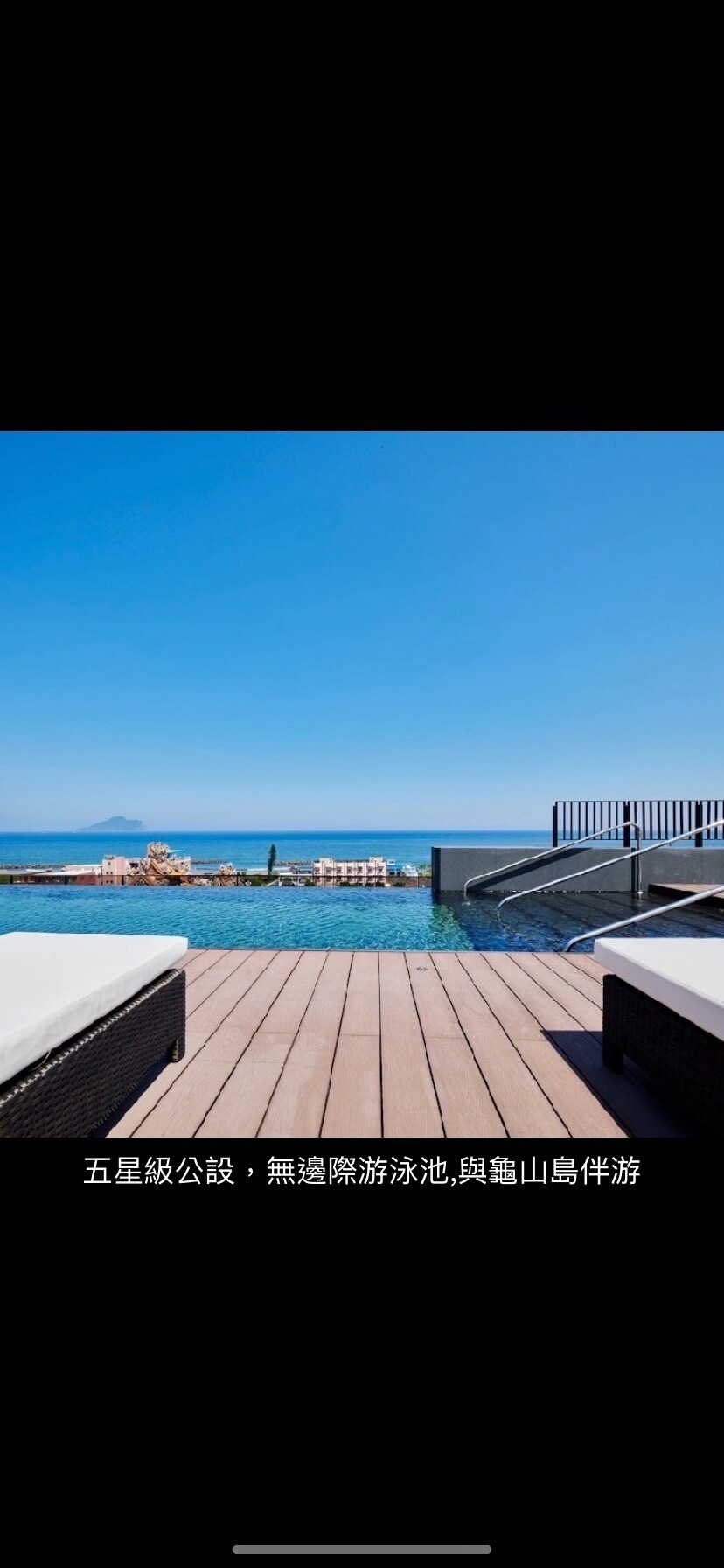 A serene view of an infinity swimming pool extends towards the horizon, inviting relaxation. The pool's edge blends into the sea, under a clear blue sky. Lounge chairs are positioned along the wooden deck, emphasizing a tranquil outdoor space.