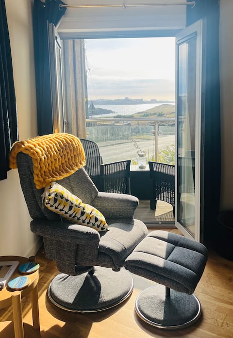Armchair with a chunky yellow throw beside the balcony doors, sea view beyond