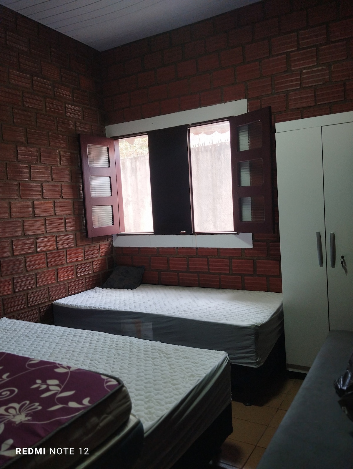 Eenvoudige kamer met sleutelkast, deurslot, bedden en ventilator aan de muur.