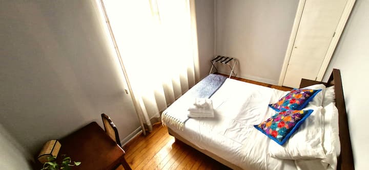 Habitación 3: la más soleada de la casa. Cama queen size con camino de cama azul pizarra y cojines bordados en azul y multicolor. La ventana con cortina de gasa deja entrar el sol del jardín.