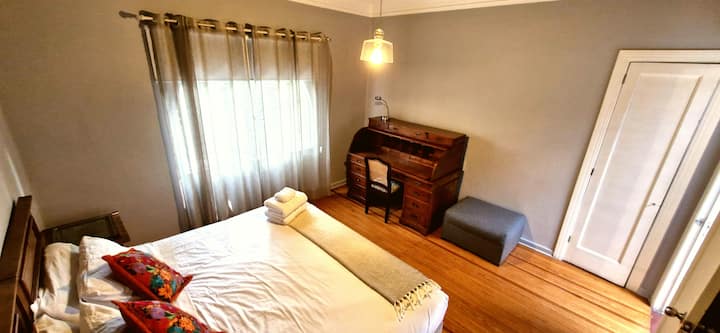 Habitación 5: una joya para los amantes de los muebles antiguos. El protagonista es un escritorio tipo buró cilíndrico de madera tallada del siglo XIX — una pieza de colección. Cama king size y vista al exterior.
