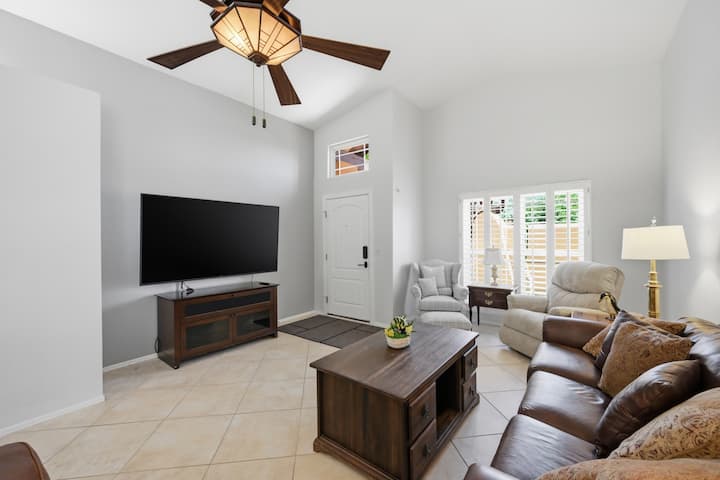This bright living space features a 75-inch smart TV, high vaulted ceilings, and abundant natural light. Comfortable seating and warm wood accents create a welcoming atmosphere, perfect for relaxing, streaming, or gathering with family and friends.