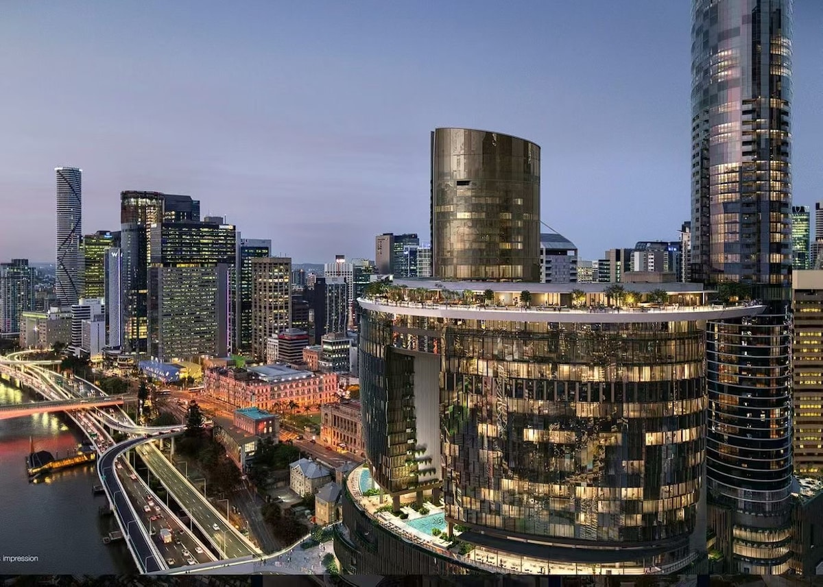 A modern urban landscape is captured at dusk, featuring a mix of low and high-rise buildings reflecting city lights. A river flows nearby, with illuminated streets adding to the vibrant atmosphere of the city.
