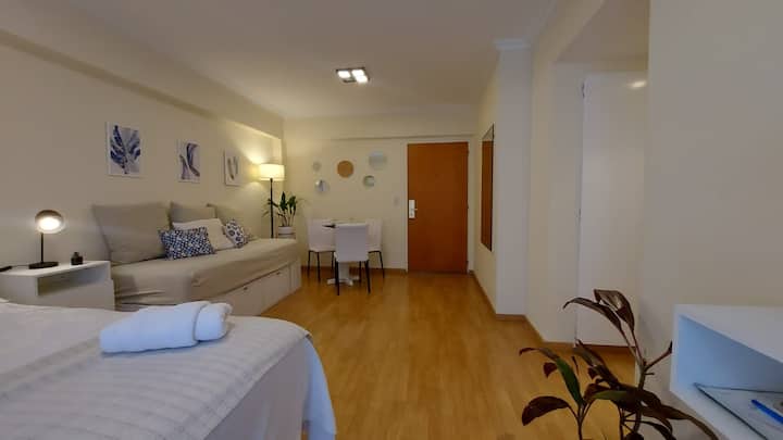 נוף לכניסה לדירה. משמאל, מיטת יחיד עם כריות שמתפקדת כספה. שולחן עם שלושה כיסאות. 