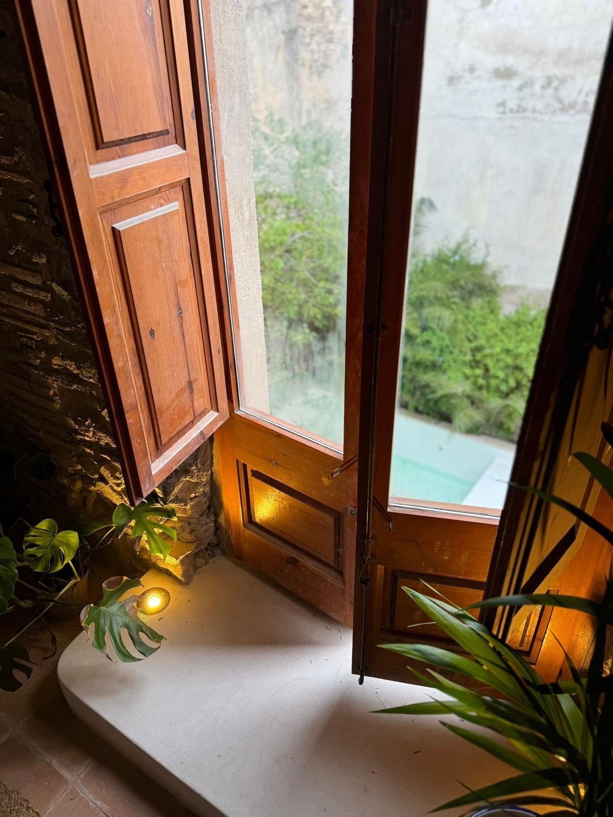 A set of wooden double doors is opened wide, revealing a glimpse of greenery in the outdoor area. Soft lighting accents the stone steps leading down, while potted plants add a touch of nature to the indoor space.
