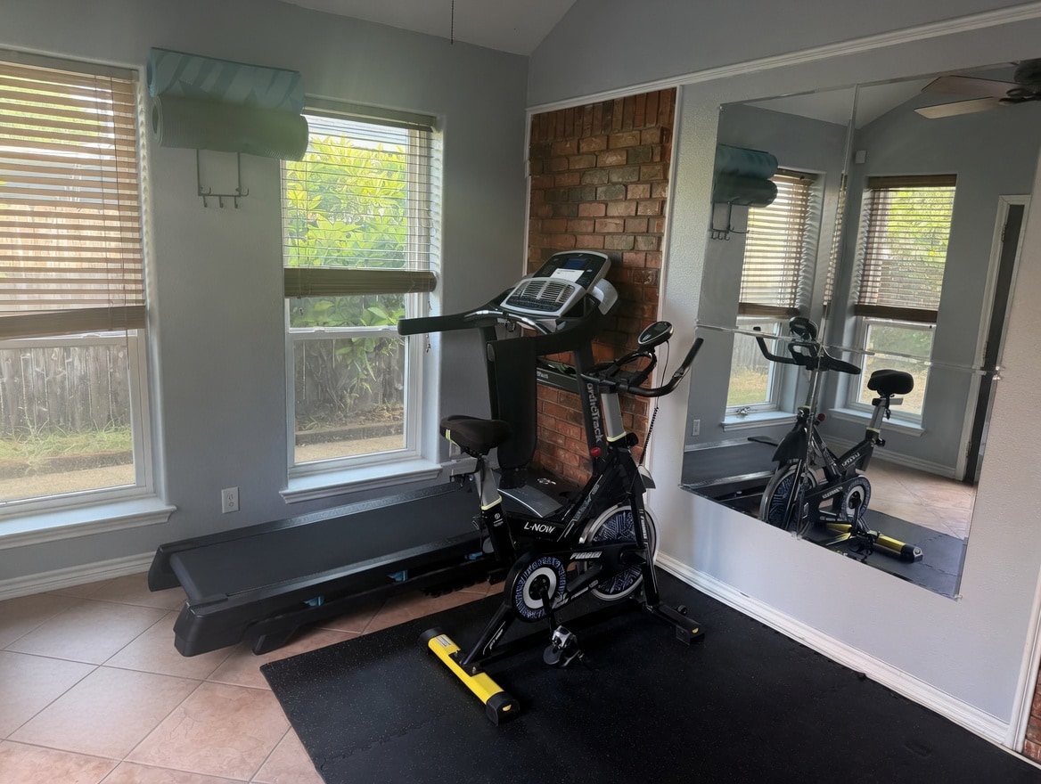 Natural-light sunroom gym equipped with a spin bike, treadmill, and yoga mats so you can skip the base gym commute.