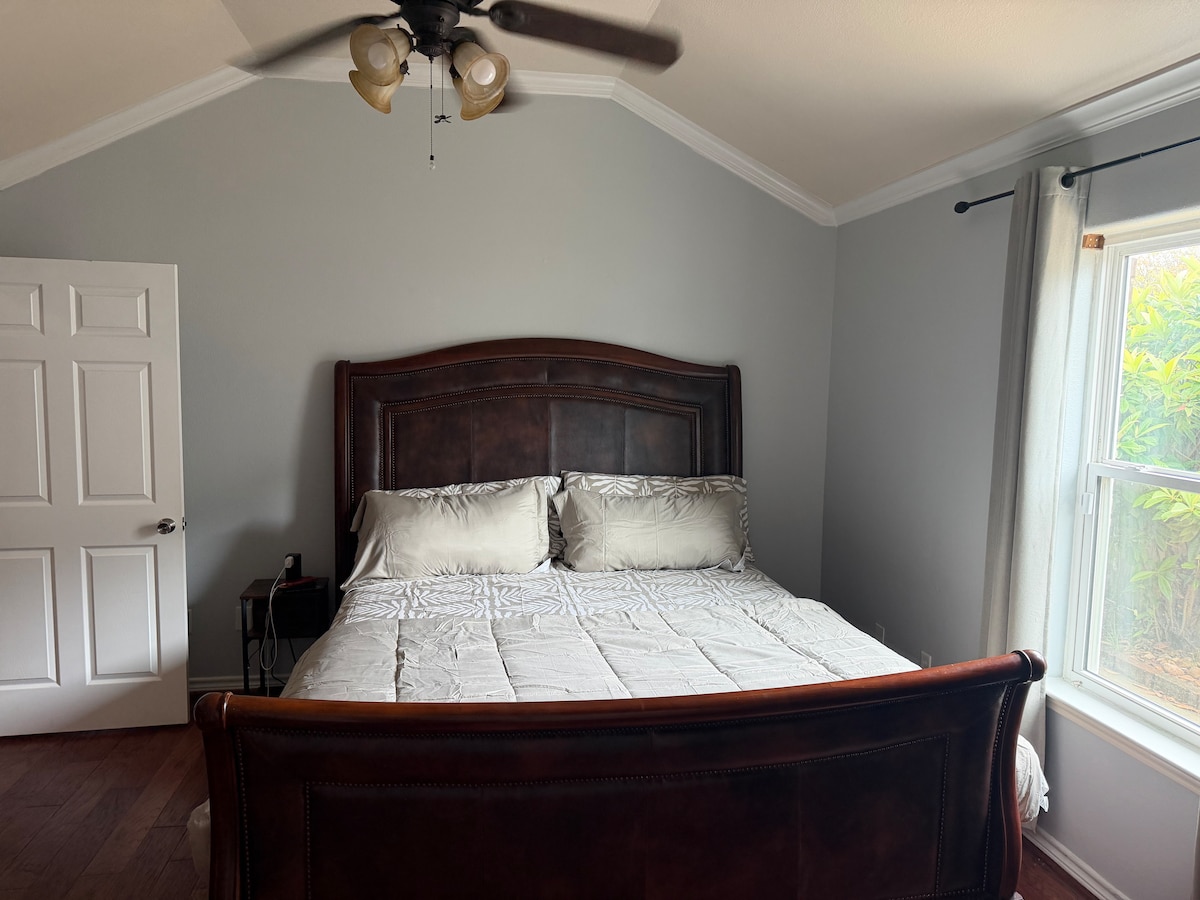 Primary suite featuring a King sleigh bed, private full ensuite bathroom, wall-mounted Smart TV, room-darkening shades, and ceiling fan.