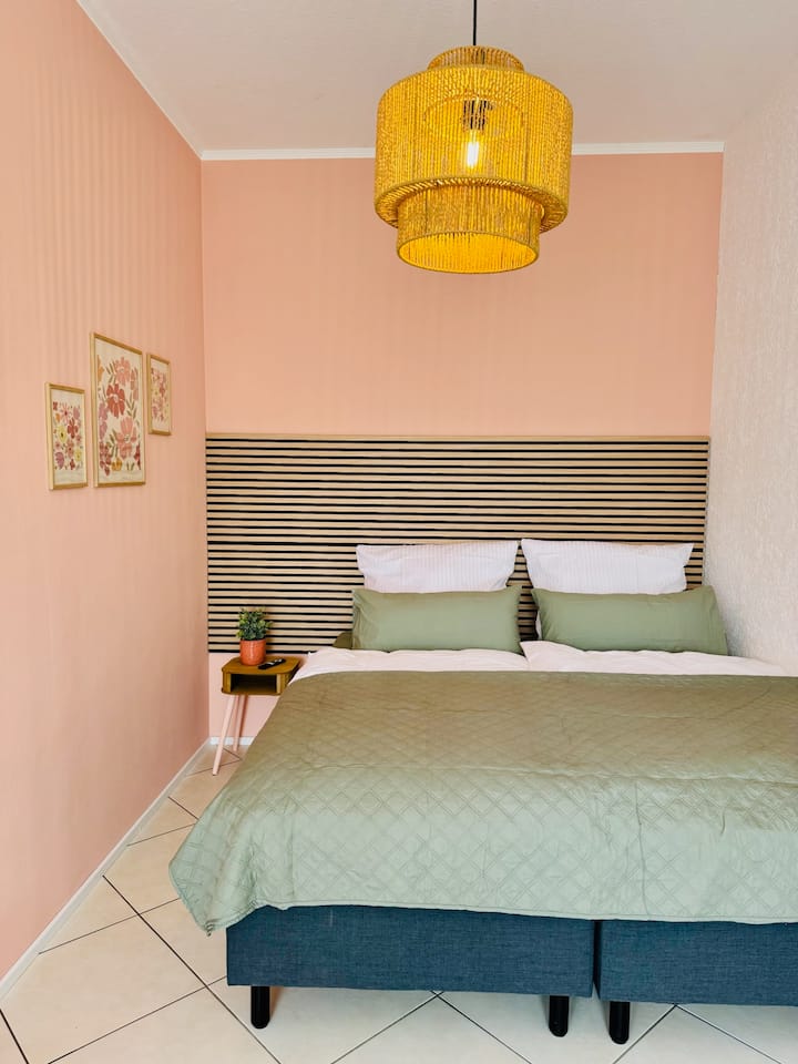 Moderno uređena spavaća soba s udobnim krevetima s oprugama, nježnim tonovima i detaljima koji podsjećaju na dom. Harmonična atmosfera poziva vas na opuštanje i osigurava dobar san – vaše utočište nakon lijepog dana.