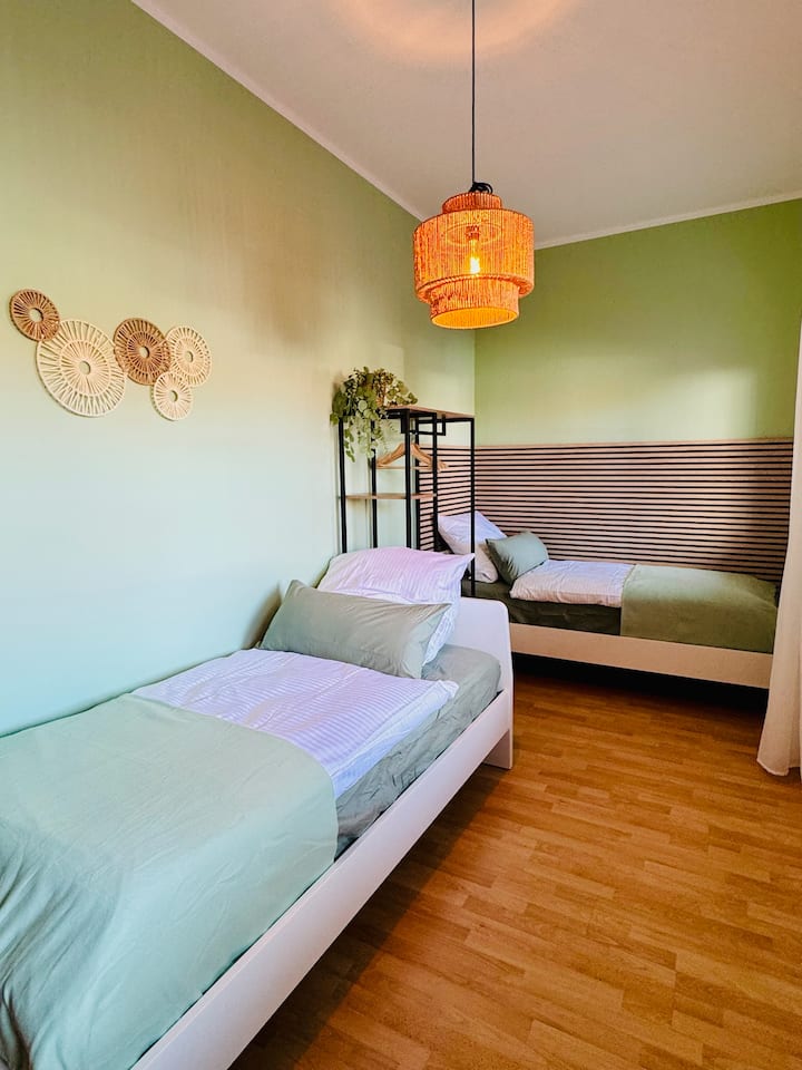 Svijetla, ugodno uređena spavaća soba s dva udobna kreveta za jednu osobu – idealno za djecu, prijatelje ili kolege. Tople boje, prirodni detalji i puno dnevnog svjetla stvaraju ugodnu atmosferu za dolazak i odmor.