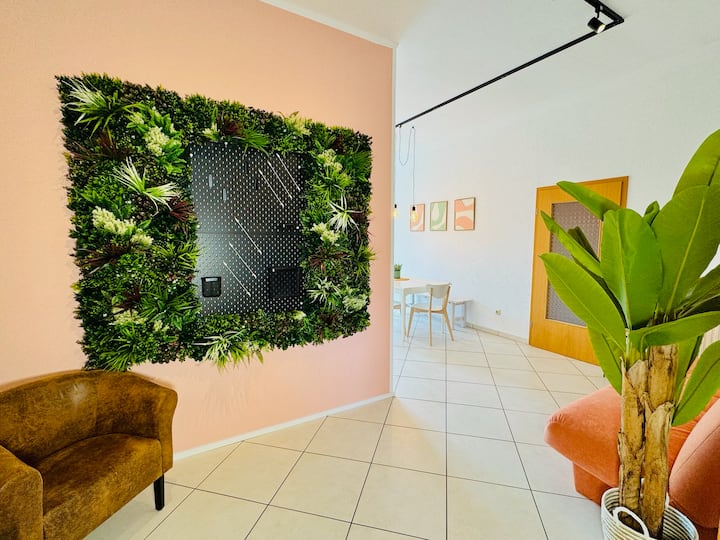 Svijetao, stilski uređen dnevni boravak s udobnom foteljom i kaučem, ukrasnim zidom s biljkama – idealan za opuštanje nakon dana ispunjenog događajima. Otvoreni dizajn stvara prijateljsku i ugodnu atmosferu.