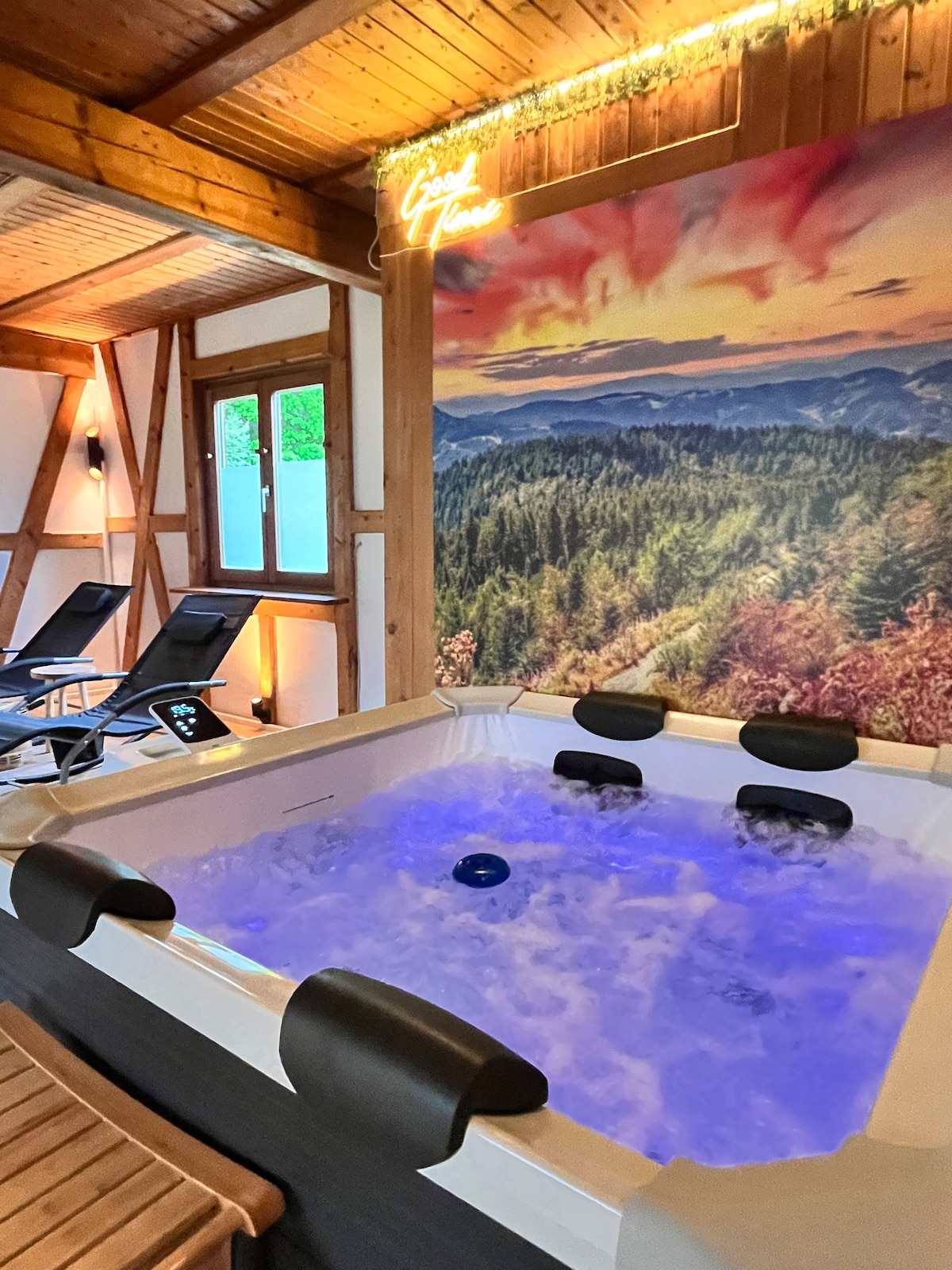 A private whirlpool is positioned in a cozy wellness area, surrounded by relaxation loungers. A natural landscape mural decorates the wall behind, featuring serene mountains and colorful foliage. Soft ambient lighting creates a calming atmosphere, inviting guests to unwind.