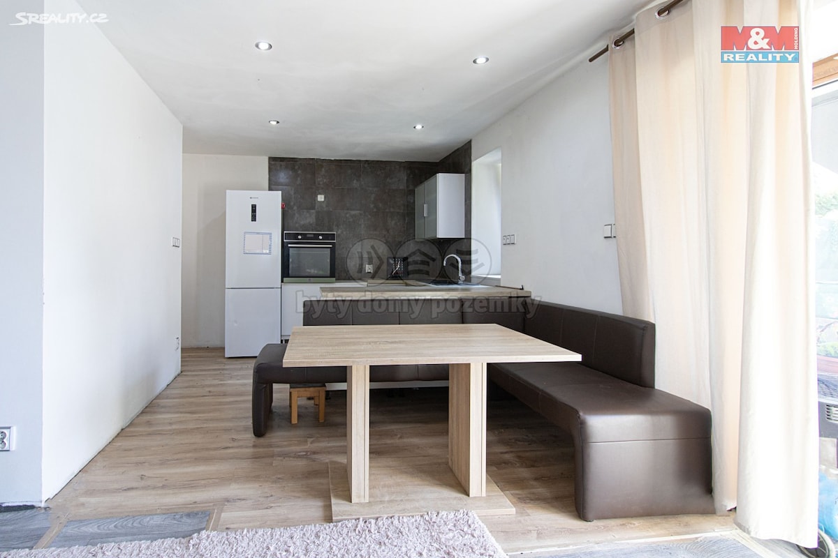 A modern dining area is featured, with a wooden table positioned centrally. A dark brown corner seating arrangement complements the table. The kitchen area is visible in the background, equipped with white cabinets and appliances that include a refrigerator and oven.