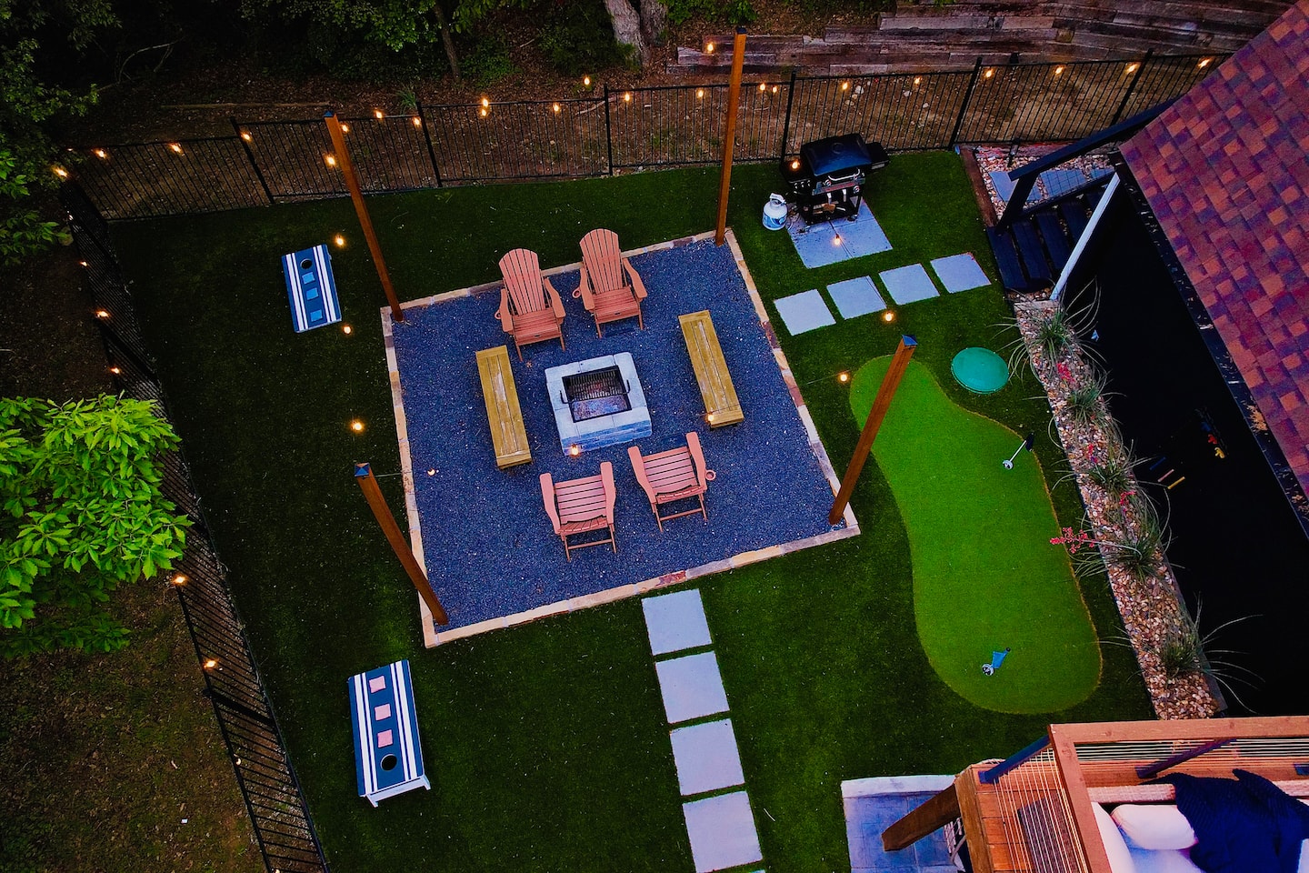 Aerial view of backyard at night — fire pit, Adirondack chairs, string lights & mini golf