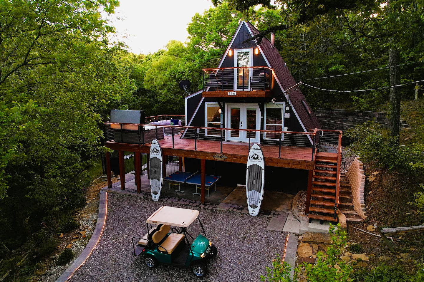 A-frame cabin exterior with golf cart, paddle boards, upper deck and wooden stairs