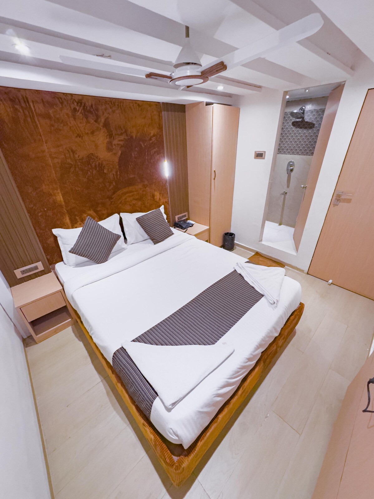 A private bedroom features a spacious bed with neatly arranged pillows and a warm tonal backdrop. Modern cabinetry complements the decor, while a sleek bathroom is visible in the corner. Soft lighting illuminates the space, creating a tranquil environment.