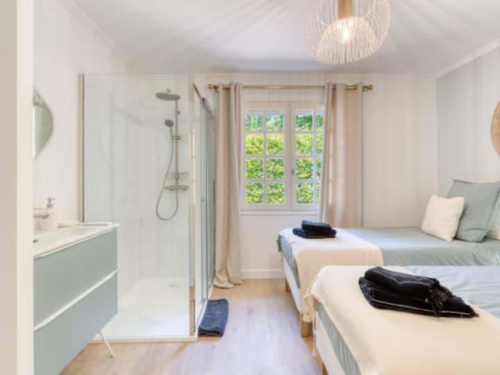 La chambre Glycine dispose de deux lits 90x180 confortables, oreillers et literie premium. Climatisation, Wi-Fi intégré et un accès une salle de bain douche privée. Dressing et tables de chevets. Idéale pour les enfants ou les amis en visite.