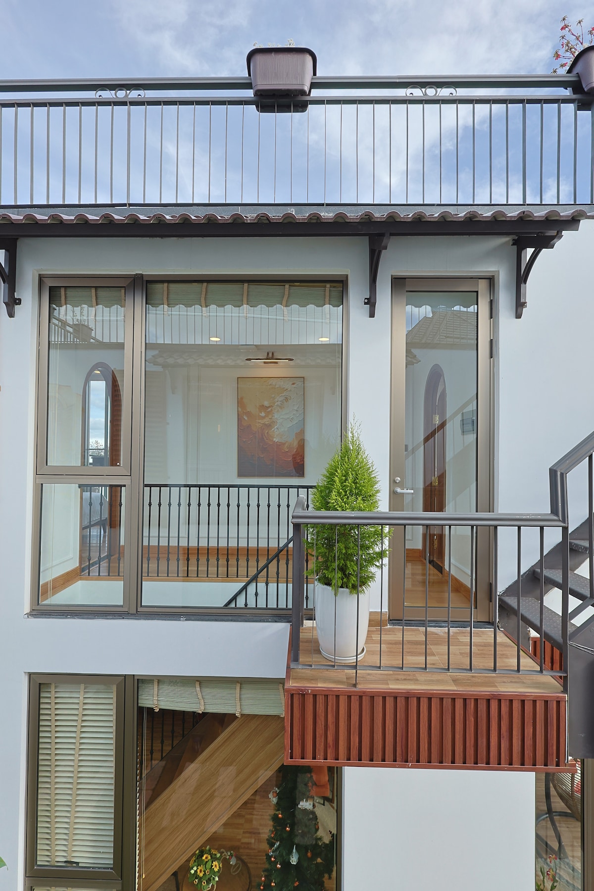 A balcony area is featured with a modern railing and a potted plant. Large glass doors provide access to the interior, while an art piece hangs on the wall, enhancing the visual appeal. The light blue exterior complements the warmth of the wood elements.