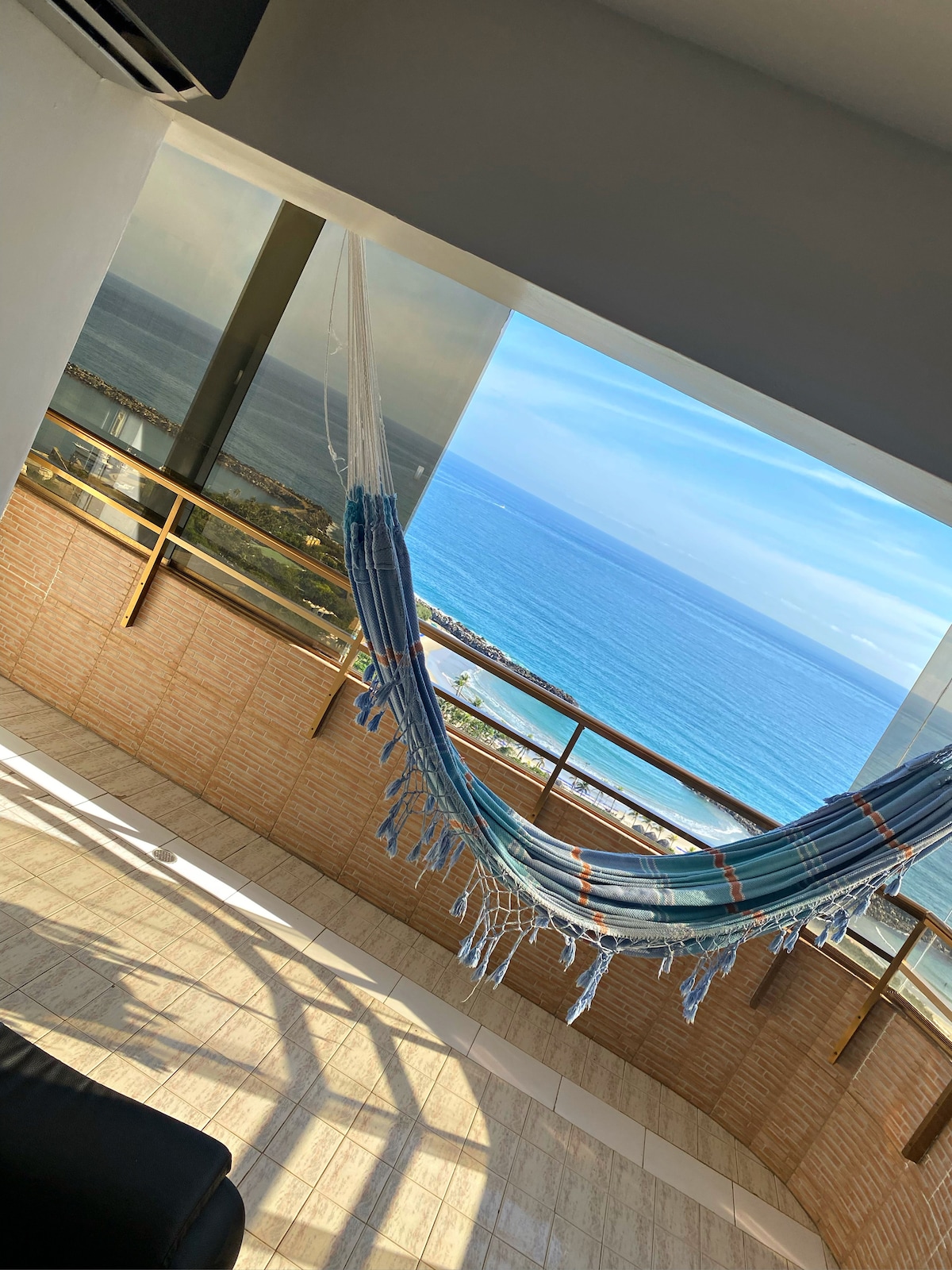 A spacious balcony features a hammock suspended between two points, offering a view of the ocean. Large glass doors allow natural light to fill the space and provide an unobstructed view of the water and sky.