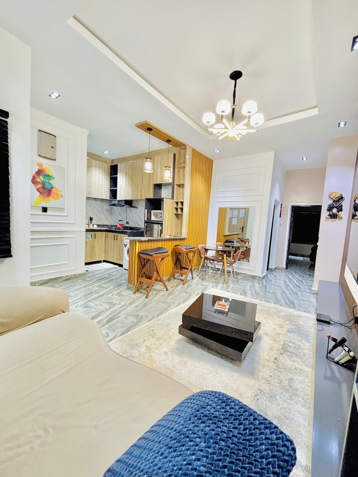 The living area features a cozy couch facing a sleek coffee table. A modern dining table with two chairs is positioned nearby. Light wood cabinetry complements the stylish kitchen, while decorative artwork adds a touch of color to the space.