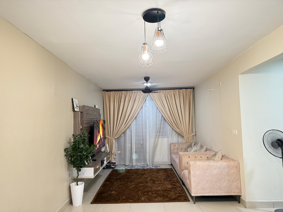 A comfortable living area is showcased with soft beige walls and a plush area rug. A light-colored sofa is positioned in front of a modern entertainment unit, which holds a TV. Sheer curtains frame a large window, while a fan provides airflow in the space.